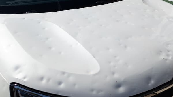 Close-up image of a car hood with visible dents and damage from hail, showing multiple small indentations across the white surface.